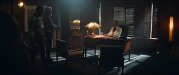Movie still from “Archenemy” (2020), directed by Adam Egypt Mortimer – A man sitting at a desk in a room; Wide shot, Over the shoulder angle