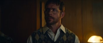 Movie still from “Archenemy” (2020), directed by Adam Egypt Mortimer – A person wearing glasses and a sweater vest; Close Up shot, Low angle
