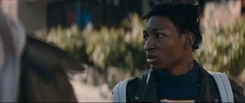Movie still from “Archenemy” (2020), directed by Adam Egypt Mortimer – A young man is looking at the camera while standing on a sidewalk; Close Up shot, Over the shoulder angle