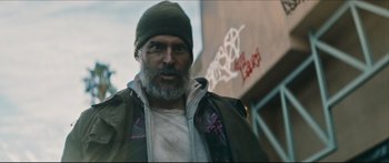 Movie still from “Archenemy” (2020), directed by Adam Egypt Mortimer – A man with a gray beard wearing a green jacket; Close Up shot, Low angle