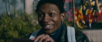 Movie still from “Archenemy” (2020), directed by Adam Egypt Mortimer – A person smiling with his hands clasped together; Close Up shot, Low angle