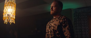 Movie still from “Archenemy” (2020), directed by Adam Egypt Mortimer – A man standing in a dark room looking up at the ceiling; Medium shot, Low angle