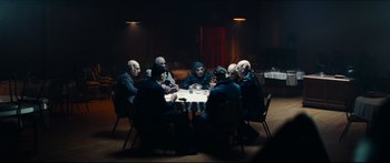 Movie still from “Archenemy” (2020), directed by Adam Egypt Mortimer – A group of people sitting around a table; Wide shot, High angle
