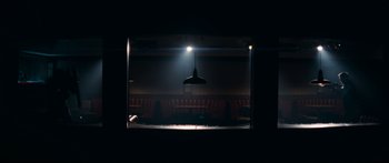 Movie still from “Archenemy” (2020), directed by Adam Egypt Mortimer – A spotlight shines on a stage in a theater; Wide shot, Low angle