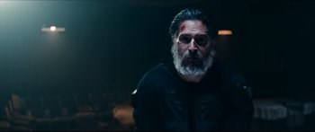 Movie still from “Archenemy” (2020), directed by Adam Egypt Mortimer – A man with a beard and a black jacket with blood on his face; Medium shot, Over the shoulder angle