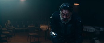 Movie still from “Archenemy” (2020), directed by Adam Egypt Mortimer – A man with a beard and a helmet is looking down; Medium shot, Low angle