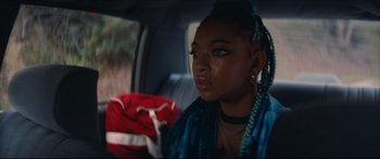 Movie still from “Archenemy” (2020), directed by Adam Egypt Mortimer – A woman with braids sitting in the back of a car; Close Up shot, Over the shoulder angle