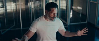 Movie still from “Archenemy” (2020), directed by Adam Egypt Mortimer – A man with a beard wearing a white t - shirt; Medium shot, Over the shoulder angle