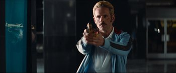 Movie still from “Archenemy” (2020), directed by Adam Egypt Mortimer – A man holding a gun while wearing a blue jacket; Medium shot, Over the shoulder angle
