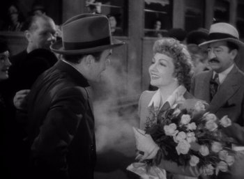 Movie still from “Arise, My Love” (1940), directed by Mitchell Leisen – A man and a woman standing next to each other holding flowers; Medium shot, High angle