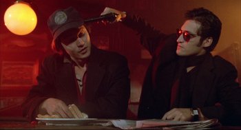 Movie still from “Arizona Dream” (1993), directed by Emir Kusturica – Two men sitting at a table in a dark room; Close Up shot, Over the shoulder angle