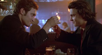 Movie still from “Arizona Dream” (1993), directed by Emir Kusturica – Two men sitting at a table arm in arm; Medium shot, Low angle