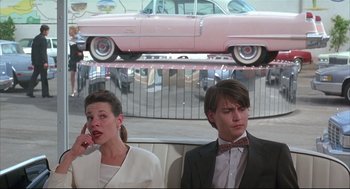 Movie still from “Arizona Dream” (1993), directed by Emir Kusturica – A man and a woman sitting next to each other in front of a pink car; Medium shot, Low angle