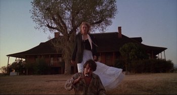 Movie still from “Arizona Dream” (1993), directed by Emir Kusturica – A woman standing on top of a man in the grass; Wide shot, Low angle