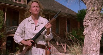 Movie still from “Arizona Dream” (1993), directed by Emir Kusturica – A woman holding a rifle in front of a brick house; Medium shot, Low angle