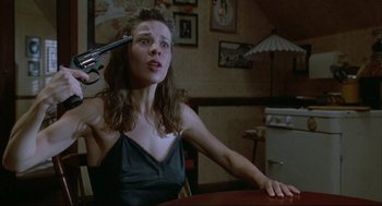 Movie still from “Arizona Dream” (1993), directed by Emir Kusturica – A woman sitting at a table with a gun in front of her head; Close Up shot, High angle