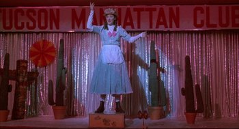 Movie still from “Arizona Dream” (1993), directed by Emir Kusturica – A woman dressed as dorothy from the wizard of oz on a stage; Wide shot, Low angle