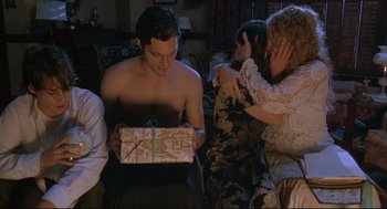 Movie still from “Arizona Dream” (1993), directed by Emir Kusturica – A shirtless man holding a present in front of a group of people; Medium shot, High angle