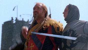 Movie still from “Army of Darkness” (1992), directed by Sam Raimi – A man with a beard and a long beard is holding a sword; Medium shot, Over the shoulder angle