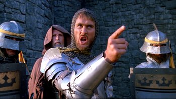 Movie still from “Army of Darkness” (1992), directed by Sam Raimi – A man dressed as a medieval knight points at something; Medium shot, Low angle