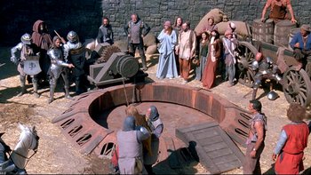 Movie still from “Army of Darkness” (1992), directed by Sam Raimi – A group of people standing around a fire pit; Wide shot, High angle