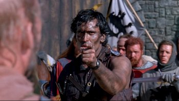 Movie still from “Army of Darkness” (1992), directed by Sam Raimi – A man in a black shirt is pointing to the camera; Close Up shot, Over the shoulder angle