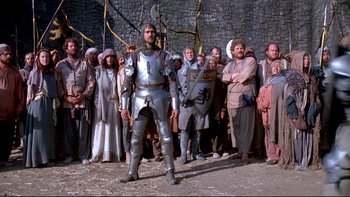 Movie still from “Army of Darkness” (1992), directed by Sam Raimi – A man dressed as a medieval knight in front of a group of people; Wide shot, Low angle