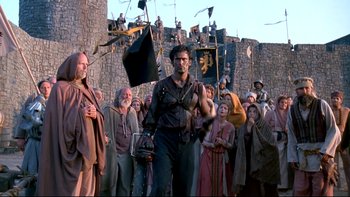 Movie still from “Army of Darkness” (1992), directed by Sam Raimi – A crowd of people standing in front of a stone wall; Wide shot, Low angle