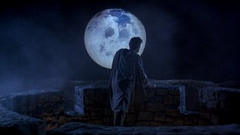 Movie still from “Army of Darkness” (1992), directed by Sam Raimi – A man standing in front of a large moon at night; Wide shot, Low angle