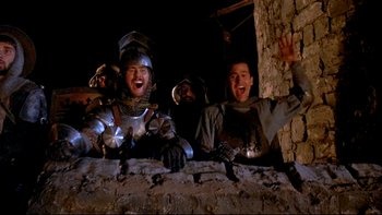 Movie still from “Army of Darkness” (1992), directed by Sam Raimi – A group of men in medieval costumes standing next to a wall; Medium shot, Low angle