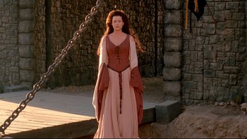 Movie still from “Army of Darkness” (1992), directed by Sam Raimi – A woman dressed in medieval clothing standing in front of a stone wall; Wide shot, High angle