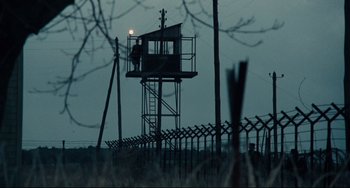 Movie still from “Army of Shadows” (1969), directed by Jean-Pierre Melville – A person standing on top of a tower next to barbed wire; Extreme Wide shot, Low angle