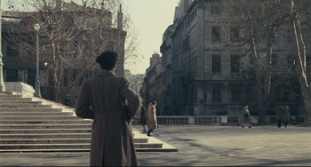 Movie still from “Army of Shadows” (1969), directed by Jean-Pierre Melville – A man in a trench coat walking down a street; Extreme Wide shot, Over the shoulder angle