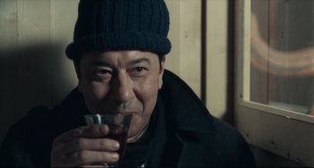 Movie still from “Army of Shadows” (1969), directed by Jean-Pierre Melville – A man wearing a hat and holding a glass of wine; Close Up shot, Low angle