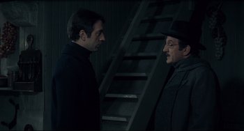 Movie still from “Army of Shadows” (1969), directed by Jean-Pierre Melville – Two men standing next to each other in front of a staircase; Medium shot, Low angle