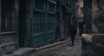 Movie still from “Army of Shadows” (1969), directed by Jean-Pierre Melville – A person walking down a street near a building; Wide shot, High angle