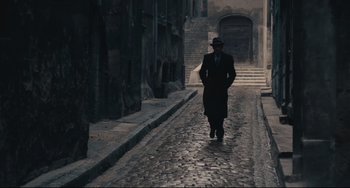 Movie still from “Army of Shadows” (1969), directed by Jean-Pierre Melville – A man walking down the street wearing a suit and a hat; Wide shot, High angle