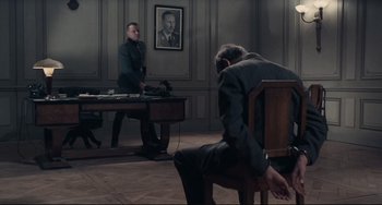 Movie still from “Army of Shadows” (1969), directed by Jean-Pierre Melville – Two men sitting in chairs in front of a desk; Wide shot, High angle