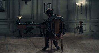 Movie still from “Army of Shadows” (1969), directed by Jean-Pierre Melville – A man sitting on a chair in a room; Wide shot, High angle