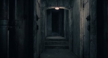 Movie still from “Army of Shadows” (1969), directed by Jean-Pierre Melville – A dark hallway with a light hanging from the ceiling; Extreme Wide shot, High angle