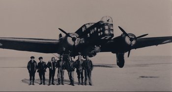 Movie still from “Army of Shadows” (1969), directed by Jean-Pierre Melville – A group of men standing in front of an airplane; Wide shot, Low angle
