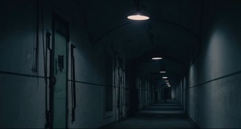 Movie still from “Army of Shadows” (1969), directed by Jean-Pierre Melville – A person is walking down a hallway in a dark room; Extreme Wide shot, High angle