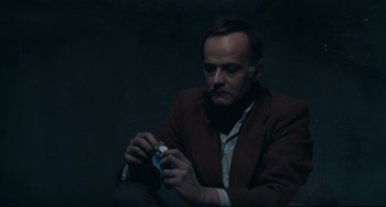 Movie still from “Army of Shadows” (1969), directed by Jean-Pierre Melville – A man sitting down holding a cigarette in his hand; Close Up shot, High angle