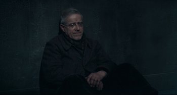 Movie still from “Army of Shadows” (1969), directed by Jean-Pierre Melville – An older man sitting on a chair in front of a wall; Medium shot, High angle