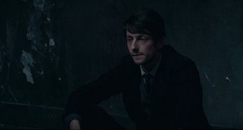 Movie still from “Army of Shadows” (1969), directed by Jean-Pierre Melville – A man in a suit sitting in a dark room; Medium shot, High angle