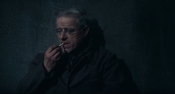 Movie still from “Army of Shadows” (1969), directed by Jean-Pierre Melville – An older man smoking a cigarette while wearing glasses; Close Up shot, High angle
