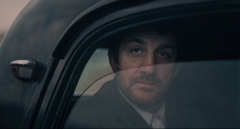 Movie still from “Army of Shadows” (1969), directed by Jean-Pierre Melville – A person wearing a suit and tie in a car; Close Up shot, Over the shoulder angle
