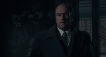 Movie still from “Army of Shadows” (1969), directed by Jean-Pierre Melville – A man in a suit and tie standing in front of a tree; Close Up shot, Low angle