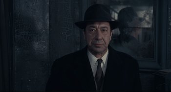 Movie still from “Army of Shadows” (1969), directed by Jean-Pierre Melville – A man wearing a suit and a hat in front of a wall; Close Up shot, Low angle