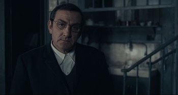 Movie still from “Army of Shadows” (1969), directed by Jean-Pierre Melville – An older man in a suit and glasses; Medium shot, Over the shoulder angle
